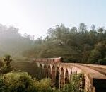 Scenic view of Nine Arches Bridge with train passing through lush greenery in Sri Lanka.
