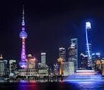 Stunning night view of Shanghai skyline with illuminated skyscrapers and the Oriental Pearl Tower reflecting in the water.